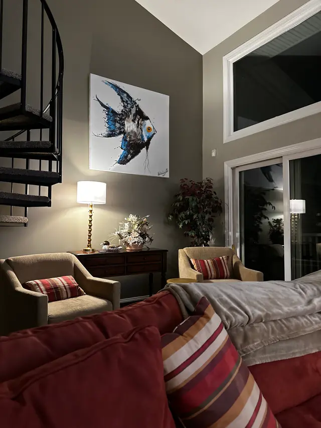 Vaulted living room with a spiral staircase, a lit table lamp, two armchairs with striped cushions and a folded throw on the sofa