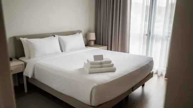 Guest bedroom reset with crisp white linen, squared pillows and a folded towel set on the bed