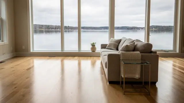 Lake house living room with a wall of windows onto a calm lake and a freshly mopped oak floor